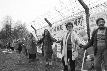 Women with linked arms surrounding nuclear test plant.