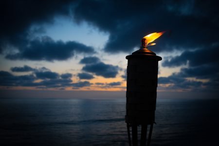 A burning torch in the night with ocean in background.