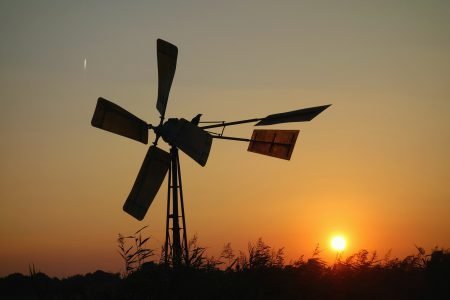 A windmill in African bush with sunset in background.