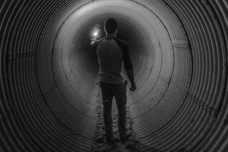 A man shining a torch/flashlight within an underground tunnel.